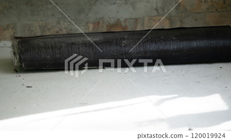 A roll of bituminous roofing material lies on a concrete floor. 120019924