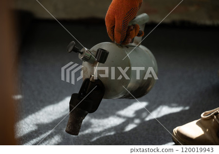 Waterproofing the floor in the house, a man heats a bitumen roll with a kerosene lamp. 120019943