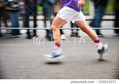 Close-up shot of runner's legs in motion, showing powerful stride as race down street, with blurred spectators in background emphasizing speed and intensity of moment. Close-up shot of runner's legs in motion, showing powerful stride as race down street, with blurred spectators in background emphasizing speed and intensity of moment. 120021071