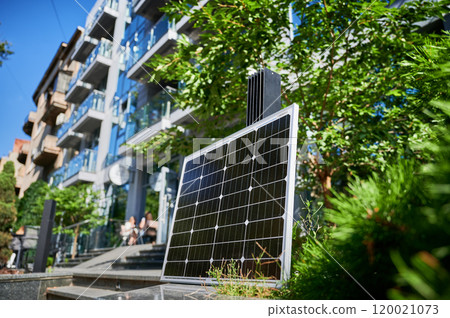 Photovoltaic solar panel in front of modern apartment building with balconies, suggesting residential or mixed-use. Concept of integration of sustainable renewable energy sources into architecture. Photovoltaic solar panel in front of modern apartment building with balconies, suggesting residential or mixed-use. Concept of integration of sustainable renewable energy sources into architecture. 120021073