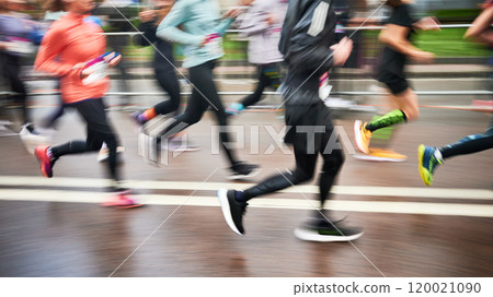 Cropped view of runners in motion blur rush down the street, colorful shoes and athletic attire creating dynamic, energetic scene as they race forward with determination. 120021090