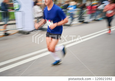Close-up shot of runner's legs in motion, showing powerful stride as race down street, with blurred spectators in background emphasizing speed and intensity of moment. 120021092