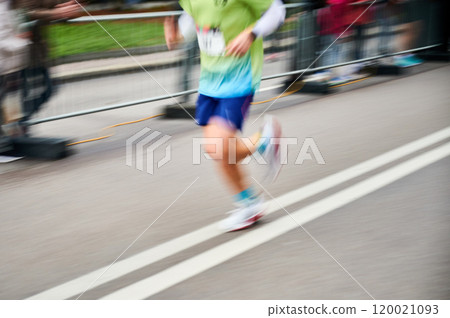 Close-up shot of runner's legs in motion, showing powerful stride as race down street, with blurred spectators in background emphasizing speed and intensity of moment. Close-up shot of runner's legs in motion, showing powerful stride as race down street, with blurred spectators in background emphasizing speed and intensity of moment. 120021093