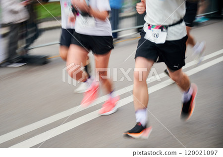 Runners in motion blur rush down the street, colorful shoes and athletic attire creating dynamic, energetic scene as they race forward with determination. Runners in motion blur rush down the street, colorful shoes and athletic attire creating dynamic, energetic scene as they race forward with determination. 120021097