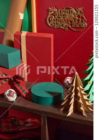 The photo with a red backdrop shows a Christmas theme from a top-down perspective, a round green platform with empty space for products on a wooden shelf, next to stacked gift boxes and paper pines. 120021155
