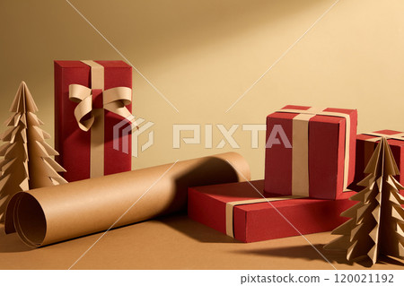 Warm Christmas themed image template on beige and brown surface, arranged with red Christmas gift boxes, paper trees, and brown paper rolls around the empty space for product display. Warm Christmas themed image template on beige and brown surface, arranged with red Christmas gift boxes, paper trees, and brown paper rolls around the empty space for product display. 120021192