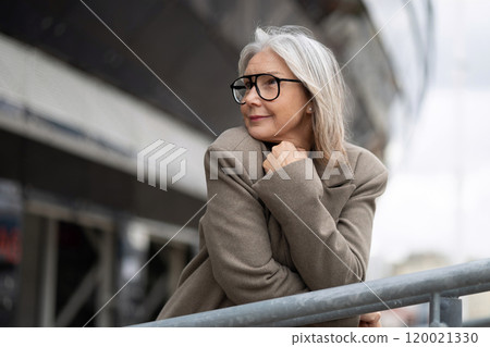 Elderly businesswoman reflects thoughtfully by the railing, showcasing a calm demeanor in an urban Elderly businesswoman reflects thoughtfully by the railing, showcasing a calm demeanor in an urban 120021330
