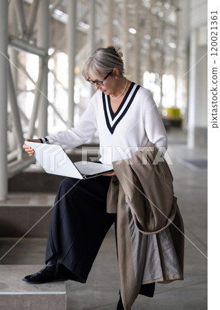 Stylish elderly woman working on her laptop in a modern building during the afternoon, dressed in a Stylish elderly woman working on her laptop in a modern building during the afternoon, dressed in a 120021361