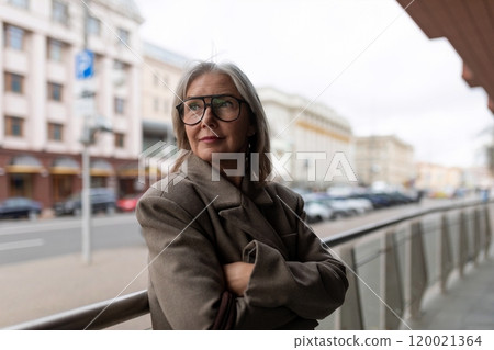 Confident middle-aged businesswoman standing on city street with arms crossed, contemplating her 120021364