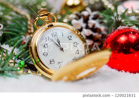 A vintage clock in the snow against the background of a Christmas tree and a garland A vintage clock in the snow against the background of a Christmas tree and a garland 120021631