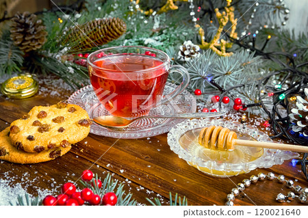 Christmas tea in glass Cup . composition with cookie, pine branches, cones on background of garlands on wooden table 120021640