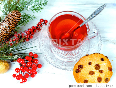 Christmas tea in glass Cup . composition with cookie, pine branches, cones on background of garlands on wooden table 120021642