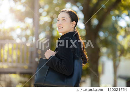 A woman going out like a business salesman in the middle of autumn and winter, with autumn leaves in the backlight 120021764