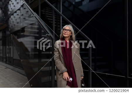 A middle-aged businesswoman standing confidently near modern stairs in an urban setting during 120021904