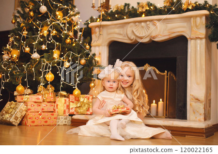 Happy children, little girls playing, gift box, Christmas tree, fireplace with holiday light at home Happy children, little girls playing, gift box, Christmas tree, fireplace with holiday light at home 120022165