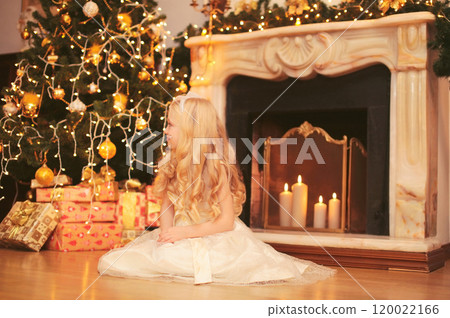 Happy little girl child with festive gift box sitting near Christmas tree and fireplace at home Happy little girl child with festive gift box sitting near Christmas tree and fireplace at home 120022166
