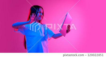 Girl waving at tablet screen, greeting with classmates, during online-lesson, with cheerful expression in neon light against vivid gradient background. Girl waving at tablet screen, greeting with classmates, during online-lesson, with cheerful expression in neon light against vivid gradient background. 120022851