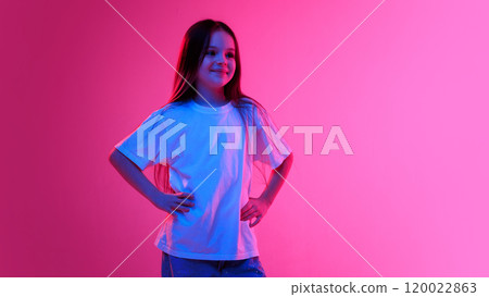 Girl in white shirt poising with hands on hips and smiling confidently in neon light against vivid gradient background. 120022863