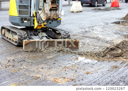 Excavator working on a busy urban road construction site during daylight hours Excavator working on a busy urban road construction site during daylight hours 120023267