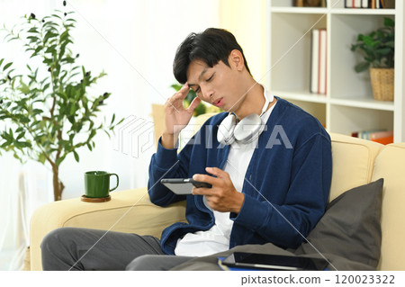 Young asian man playing a video game on smartphone feeling upset after loosing 120023322