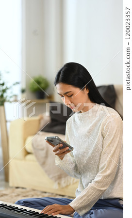 Happy young asian woman checking social media on smartphone at home 120023357