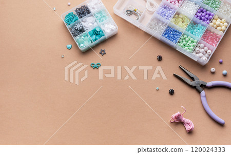 Crafting with colorful beads on a flat workspace with tools and containers in bright daylight Crafting with colorful beads on a flat workspace with tools and containers in bright daylight 120024333