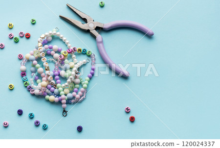 Colorful assortment of beads and jewelry-making tools on a blue surface with completed bracelets 120024337
