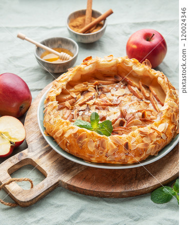 Delicious homemade apple tart displayed on a wooden board surrounded by fresh apples and honey 120024346