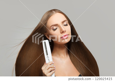 Perfect smiling woman with long straight healthy hairstyle using straightening iron  120025415