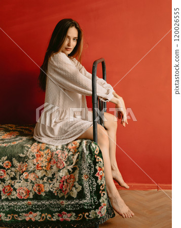Beautiful woman with natural flawless skin, wearing vintage style dress sitting on retro bed. Fashion concept 120026555