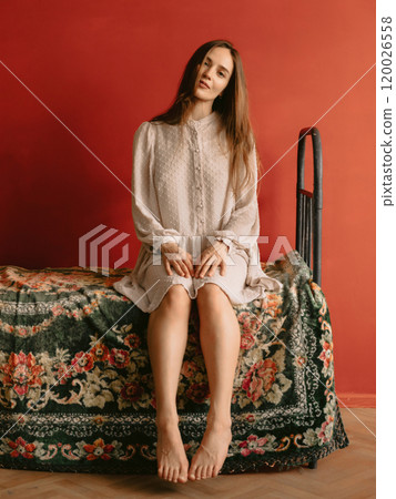 Beautiful woman with natural flawless skin, wearing vintage style dress sitting on retro bed. Fashion concept Beautiful woman with natural flawless skin, wearing vintage style dress sitting on retro bed. Fashion concept 120026558