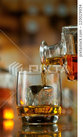 Freeze motion of pouring whisky into glass . Bar with bottles on background. 120029934