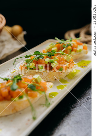 Gourmet bruschetta topped with salmon tartare, avocado, and microgreens, drizzled with olive oil 120030265