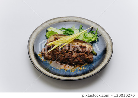 Braised meat served with roasted eggplant, greens, and fresh garnish for elegant and flavorful dish 120030270