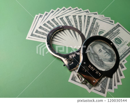 Closeup banknotes and metal hand cuff on a green background. Closeup banknotes and metal hand cuff on a green background. 120030544