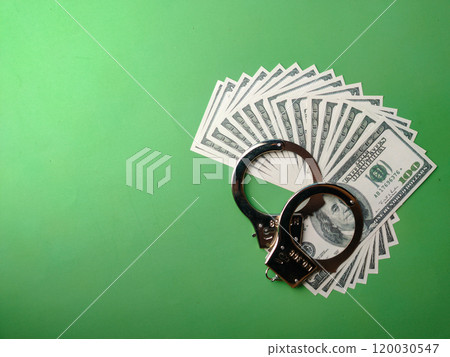 Top view banknotes and metal hand cuff on a green background with copy space. Top view banknotes and metal hand cuff on a green background with copy space. 120030547