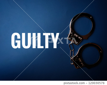Top view metal hand cuff with text GUILTY on a blue background. 120030578