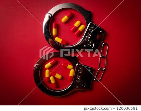 Top view metal hand cuff and medical pill on a red background. 120030581