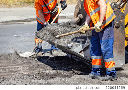 Construction workers repairing a city road under bright sunlight with machinery and tools 120031269