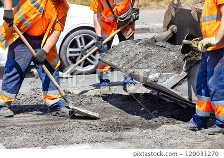 Workers repairing a road with asphalt under the midday sun in an urban setting 120031270
