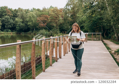 Stylish hipster woman holding paper map, wearing backpack and relaxing in nature. Travel and wanderlust concept. Amazing chill moment, summer time 120032284
