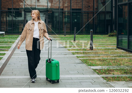 Cheerful young woman in casual outfit walking on the city park with green luggage. 30s Woman dragging suitcase near hotel. Travel Fashion concept. Full body Cheerful young woman in casual outfit walking on the city park with green luggage. 30s Woman dragging suitcase near hotel. Travel Fashion concept. Full body 120032292