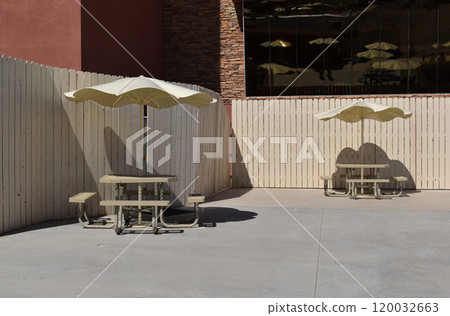 Empty benches and a table under parasol, beige sun umbrella against the background of a beige fence Empty benches and a table under parasol, beige sun umbrella against the background of a beige fence 120032663
