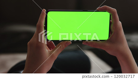 Young woman lying on a couch and using smartphone with horizontal green screen 120032717