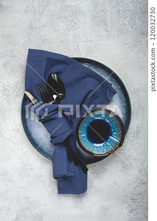 food background, with an empty blue plate, a bowl, black cutlery, with a napkin, on a gray background, table setting, top view, no people, 120032730
