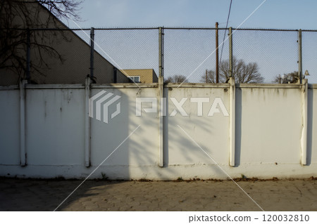 White wall with chain-link fence and shadows in an urban environment 120032810