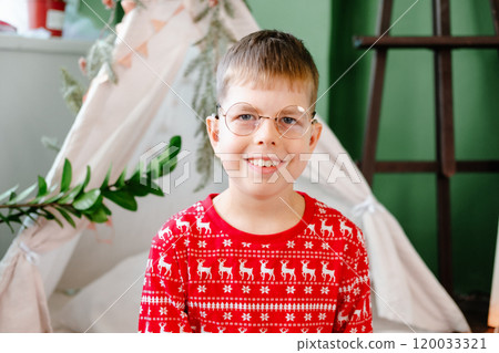 funny boy with glasses and red pajamas smiles widely against the backdrop of a fabric wigwam in his bedroom 120033321