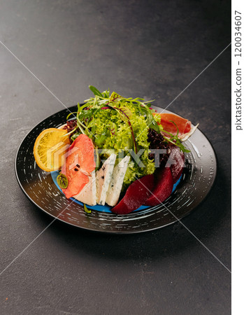 Fresh gourmet salad with greens, blue cheese, citrus, and dried fruit on a stylish black plate 120034607