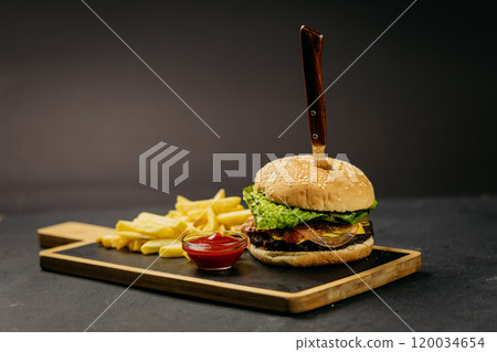 Classic burger with fresh lettuce and tomato served with crispy fries and ketchup on a wooden board Classic burger with fresh lettuce and tomato served with crispy fries and ketchup on a wooden board 120034654