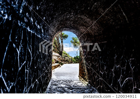 View from inside a tunnel to a green landscape with trees and blue sky. Passage to a beach 120034911